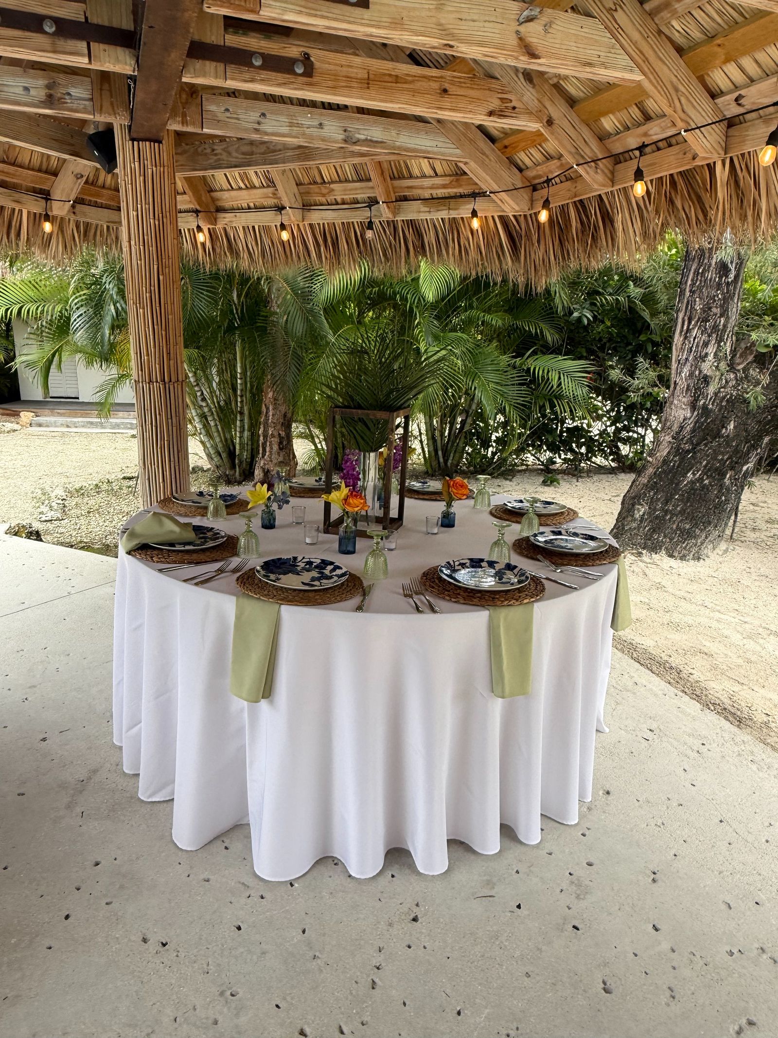Elegant round table setting under tiki hut with string lights